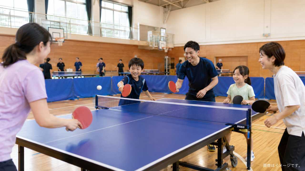 米子市の明るい体育館で、卓球台を囲んで初心者と家族が楽しそうにラリーをしている写真