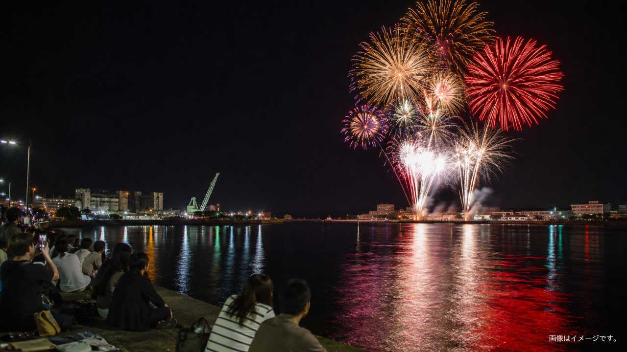 夜の境水道沿いで花火を眺める人々と海面に映る光