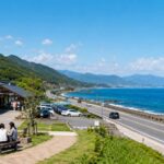 鳥取県の海沿いを走るドライブ風景と、清潔感のある道の駅、青い日本海、遠くに山並み、旅行者が休憩している様子