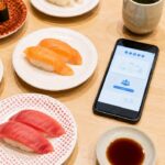 鳥取の回転すし北海道の予約方法を調べるスマートフォンと寿司皿を並べた食卓