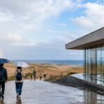 雨の鳥取観光を象徴する砂丘と屋内ミュージアムを背景に傘を持つ旅行者が立つ構図